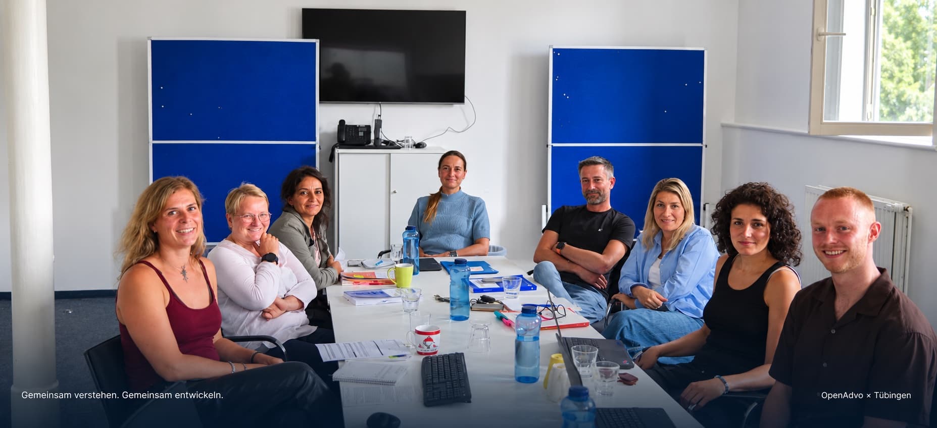 Workshop mit der Stadt Tübingen: Mitarbeitende der Stadt und das OpenAdvo-Team am Besprechungstisch. Bildtext: „Gemeinsam verstehen. Gemeinsam entwickeln.“ – OpenAdvo × Tübingen